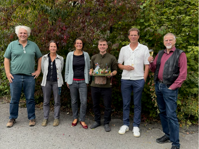 Five people pose in nature holding a PhD hat, smiling.