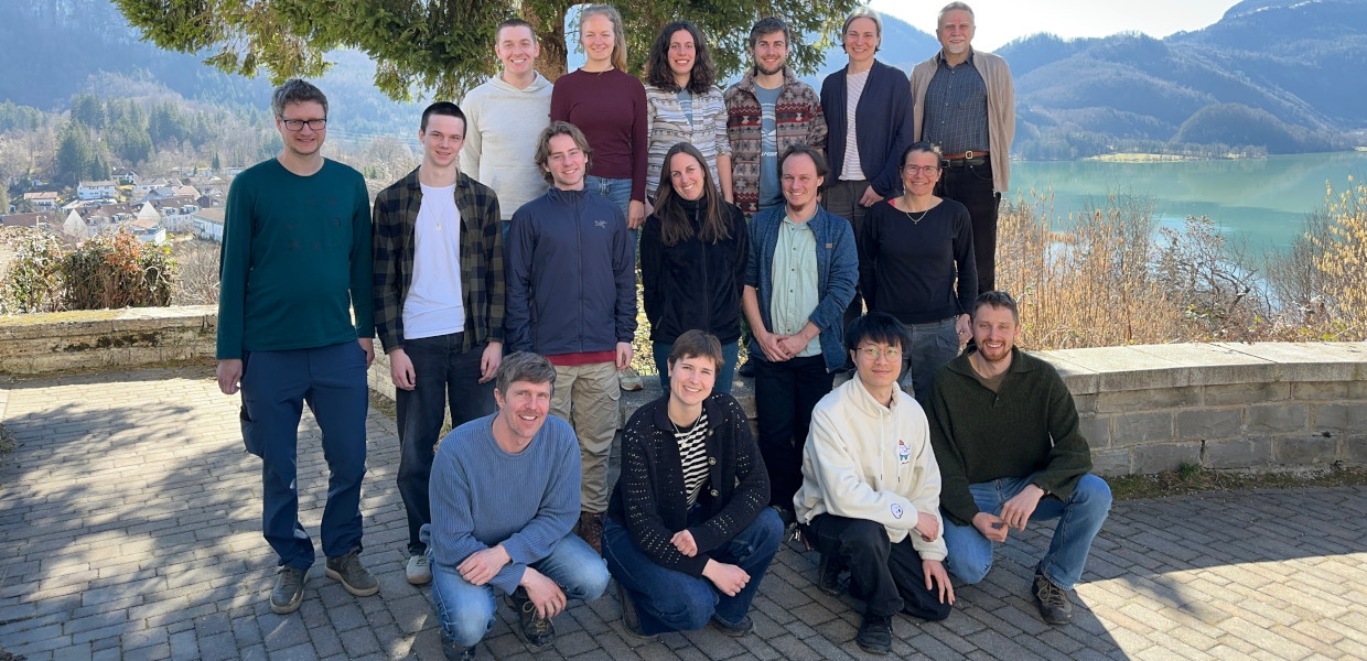 Nadine Ruehr, KIT Plant ecophysiology working group standing and kneeling, in the background hills and lake Kochel